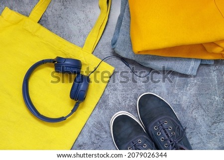 orange clothes and jeans blue headphones is a yellow bag with a glass of background. top view