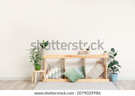 Wooden TV stand with pillows and houseplants near light wall