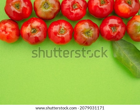 Top view of ripe red acerola cherries and green leaves isolated on a light green background. High vitamin C and antioxidant fruits. Space for text. Close-up photo. Healthy fruits concept