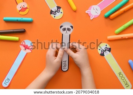Hands of child with cute bookmarks and markers on color background