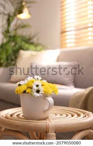 Cup with beautiful bright flowers on table in living room