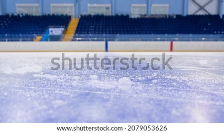Clean empty ice hockey rink. Skate blade marks and snow crumbs. Empty stands in background.