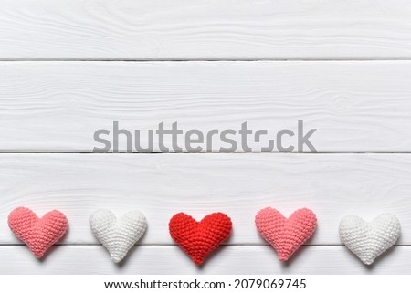 A banner for Valentine's Day with knitted hearts in a row on the right side on a white wooden background. February 14. Copy space. Flat lay, top view.