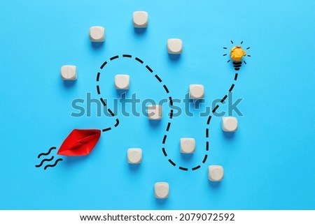 To overcome obstacles and to find a creative idea in business or education concept. Red paper boat finds a way to reach the light bulb by passing through the obstacles. Royalty-Free Stock Photo #2079072592