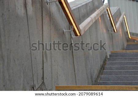 from the bottom of the handle is a recessed LED strip with yellow light. hidden built-in lamp shows a man's hand. the concrete side of the staircase with retaining walls runs through terrain of slope Royalty-Free Stock Photo #2079089614