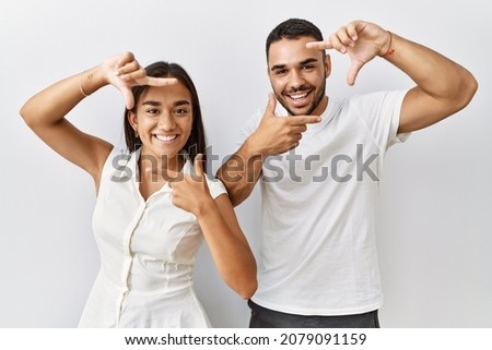 Young interracial couple standing together in love over isolated background smiling making frame with hands and fingers with happy face. creativity and photography concept. 