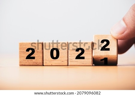 Hand flipping wooden block cube flipping between 2021 to 2022 with bokeh background for change and preparation merry Christmas and happy new year.