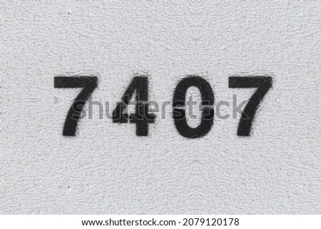 Black Number 7407 on the white wall. Spray paint. Number seven thousand four hundred and seven.