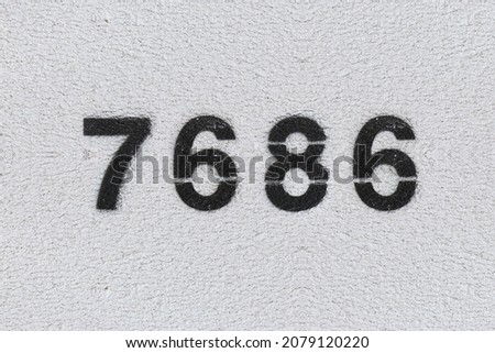 Black Number 7686 on the white wall. Spray paint. Number seven thousand six hundred and eighty six.