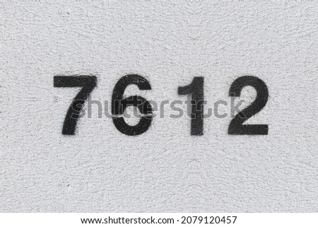 Black Number 7612 on the white wall. Spray paint. Number seven thousand six hundred and twelve.