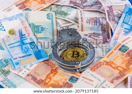 bitcoin shiner chained with handcuffs on russian paper rubles currency background - crypto ban law concept