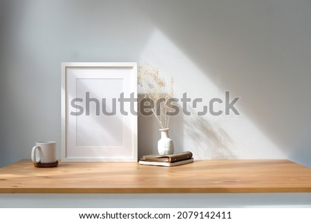 White empty picture frame, coffee cup and potted plant on wooden table near window.