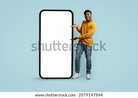Cheerful african american millennial man showing huge modern cellphone with blank screen, showing newest entertaining or dating mobile app, mockup, blue studio background, copy space Royalty-Free Stock Photo #2079147844