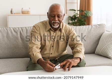 Sick Mature African Male Using Pulse Oximeter Measuring Saturation Level With Medical Device Siting On Sofa At Home. Pulseoxymetry, Coronavirus Disease In Older Age Concept Royalty-Free Stock Photo #2079147949