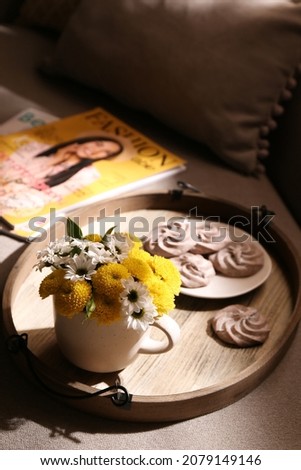 Tray with flowers in cup and delicious cookies on sofa indoors