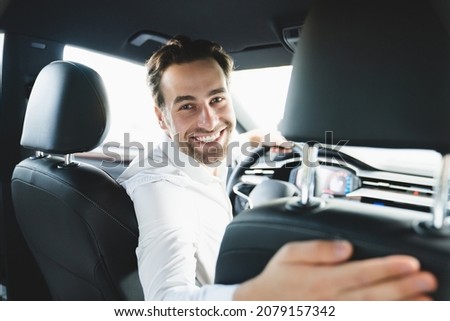 Taxi driver smiling while turning over to the backseat looking talking with clients. Successful businessman husband looking at the backseat at dealer shop before buying a car Royalty-Free Stock Photo #2079157342