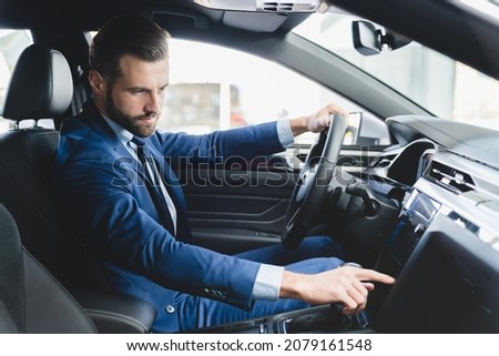 Confident caucasian businessman in formal clothes trying checking new car starting engine before buying purchasing it at automobile dealer shop Royalty-Free Stock Photo #2079161548