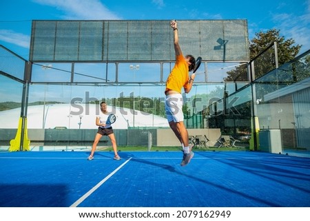 Mixed padel match in a blue grass padel court - Beautiful girl and handsome man playing padel outdoor Royalty-Free Stock Photo #2079162949
