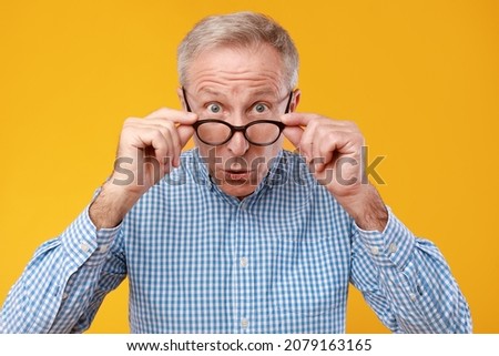 Wow, Omg. Closeup portrait of surprised amazed mature man looking staring at camera taking off eyeglasses, shocked by news or special offer, standing isolated on yellow orange studio background Royalty-Free Stock Photo #2079163165