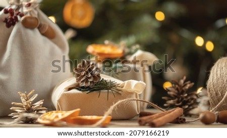 Zero waste christmas concept. Packed in natural fabric gifts and decorations from natural materials on wooden table near Christmas tree with lights