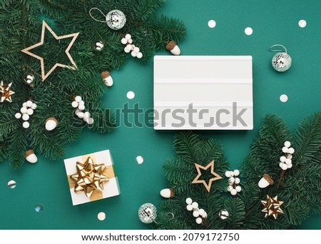 Happy New Year concept. Empty white Lightbox with gift box, holiday silver gold decorations, acorns on green Christmas tree branches background. Flat lay, top view, copy space. Festive winter time.