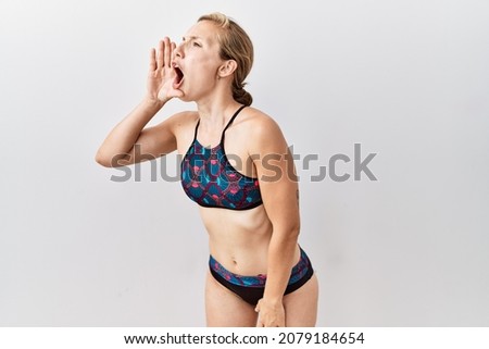 Young blonde woman wearing sporty bikini over isolated background shouting and screaming loud to side with hand on mouth. communication concept. 