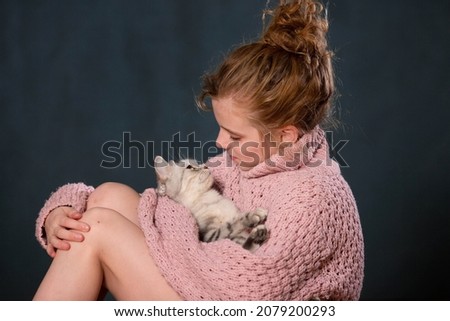 cute young girl with gray cat together on a dark background
