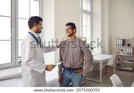 Happy, smiling young man talking to his doctor. Qualified specialist at a modern clinic, hospital or medical center reassuring his male patient after a consultation and health checkup Royalty-Free Stock Photo #2079200701