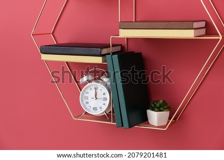 Shelf with books and alarm clock hanging on color wall, closeup