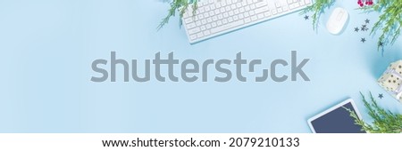 Simple minimal Christmas office background. Modern high-colored light blue background with office pc keyboard, mouse, tablet pc, silver festive stars and christmas tree branches, flatlay frame