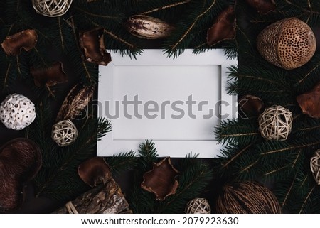 Empty picture frame with pine tree and natural christmas decoration on dark brown background. Flat lay minimal new year mockup template. Creative styled image composition with organic christmas bauble