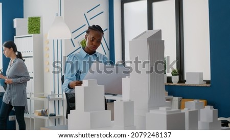 Woman builder analyzing blueprints plans to design layout of construction site and building model. Architect using maquette and property structure to build urban real estate project. Royalty-Free Stock Photo #2079248137