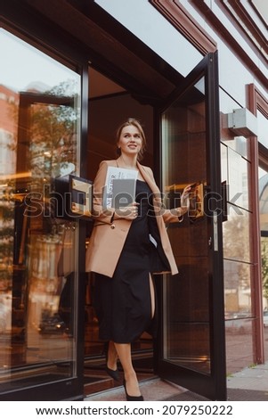 Young well dressed smiling business woman with tablet pc leaving building, summer day outdoors Royalty-Free Stock Photo #2079250222