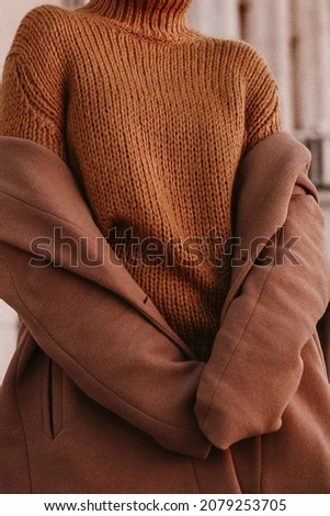 Cropped female figure in a brown cozy warm coat and knitted orange sweater. Street casual winter or autumn fashion.