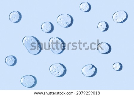 Cosmetic hydrating product or ingredient concept. Blue drops of transparent liquid on a light background. Drops gel or oil close up. Abstract backdrop. Royalty-Free Stock Photo #2079259018