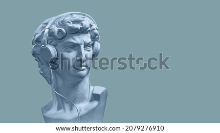 Bust of Michelangelo's David wearing a blue mask and headphones on an isolated blue-gray background. A place to copy the text. The concept of minimalism Royalty-Free Stock Photo #2079276910