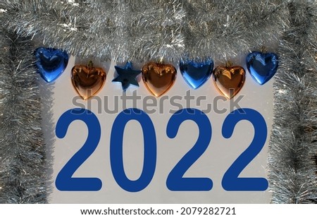 Christmas banner with the inscription in blue 2022, on a gray background with a shiny garland and toys. Poster design with place for an inscription.