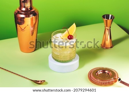 Whiskey sour popular alcoholic cocktail with bourbon, lemon juice, egg white and ice, rocks glass on bright green background