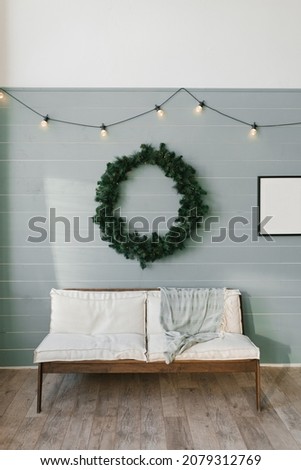Wooden sofa with white soft pillows and a large Christmas wreath on the wall, lined with clapboard