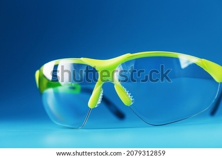 Transparent polycarbonate safety glasses on a blue background. Reliable eye protection, free space