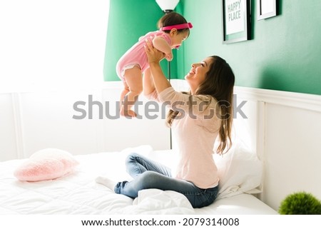 Excited caucasian mom lifting her happy baby girl in her arms and playing while making her daughter laugh 