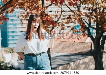 Portrait of a young woman in park pointing a copy space to put text or image. White tshirt clothes blank space. Redhead beauty body positive girl. Colorful background copy space