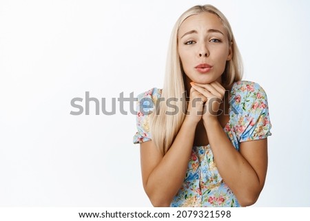 Image of cute blond girl yearning for something cute, looking with affection, tempted face expression, standing over white background