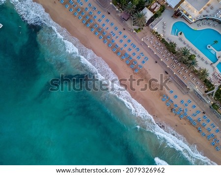 Aerial view of sun loungers between resort city and blue sea