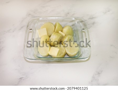 Top view of pieces of boiled potatoes on a baking dish topped with butter and kosher salt to make mashed potatoes for thanksgiving dinner.