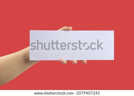 Hand holding blank white paper label on red background. With copy space.