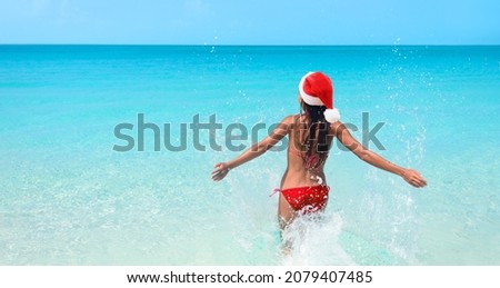 Christmas fun happy bikini woman swimming in paradise turquoise beach ocean wearing santa hat happy with open arms. Dream destination for Xmas holidays getaway. Panoramic banner.