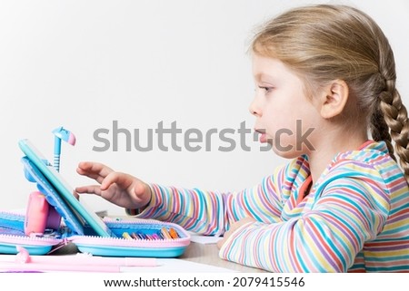 The girl is engaged in online education on the tablet at the table in the children's room. Child and gadget. Watching cartoons, reading, chatting, listening to music, playing on your tablet