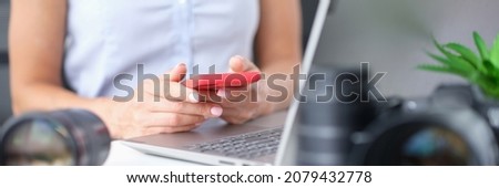 Woman holds smartphone in hands on table stands laptop near lens from camera Earning money from stock photography concept