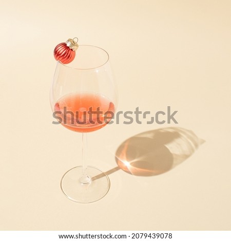 Minimal composition with rose vine glass and Christmas baubles on bright cream background. Creative party concept.